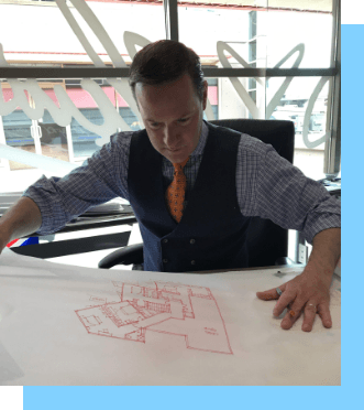 Man looking at map of house while wearing a blue vest and an orange tie